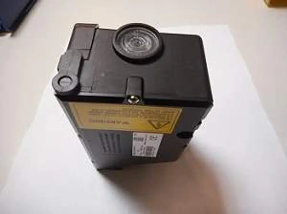 Schwarzes Steuergerät von Remeha mit rundem Sichtfenster und gelber Warnlabels. An der Vorderseite sind einige technische Informationen und ein Barcode sichtbar.